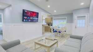A modern living room with a flat-screen TV mounted on the wall, a glass coffee table, and a sofa. - Bright & airy 2BR, 2BA beach retreat A (North Myrtle Beach)