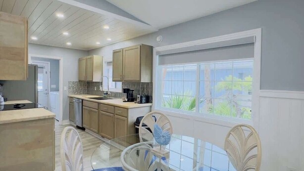 A modern kitchen with wooden cabinets, a glass dining table, and a view of greenery outside. - Bright & airy 2BR, 2BA beach retreat A (North Myrtle Beach)