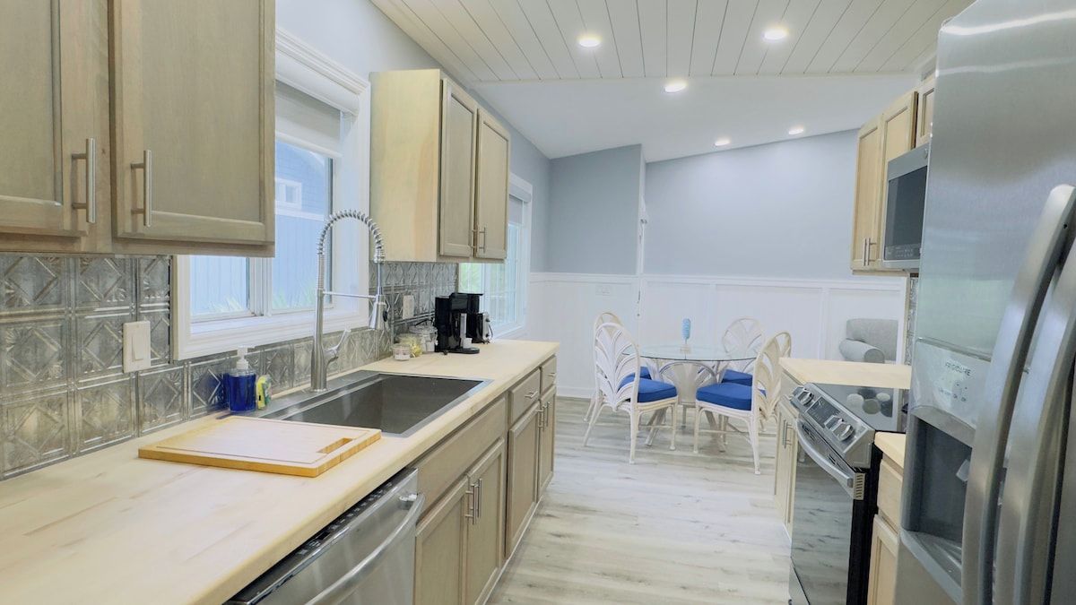 A modern kitchen with a built-in oven, a stainless steel refrigerator, and a dining area with a white table and blue chairs.