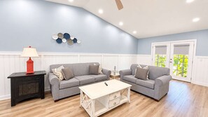 A living room with two grey sofas, a white coffee table, a red lamp, and a wall with decorative plates. - Bright & airy 2BR, 2BA beach retreat A (North Myrtle Beach)