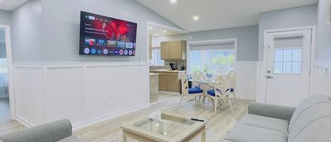 Una sala de estar moderna con un televisor de pantalla plana montado en la pared, una mesa de centro de vidrio y un rincón de descanso con sofás y sillones.