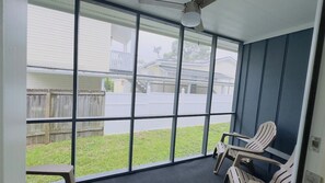 A covered porch with large windows, a ceiling fan, and two chairs.