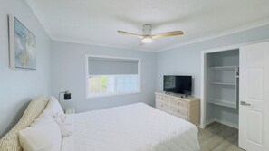 Un dormitorio con cama, televisión, armario y ventilador de techo.