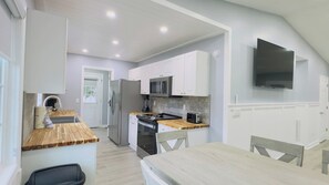 Una cocina moderna con armarios blancos, microondas, refrigerador y encimera de madera.