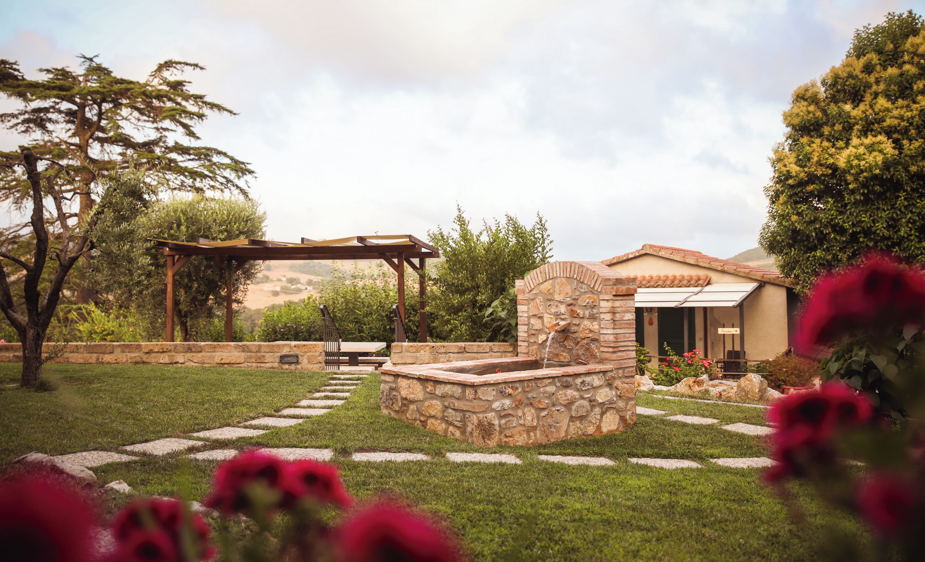 A stone fountain, a pergola, and a stone wall in a garden.