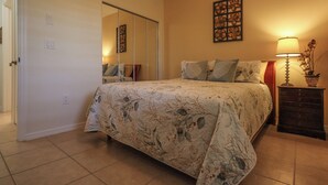 Un dormitorio con cama, mesita de noche, lámpara, espejo y una obra de arte en la pared.