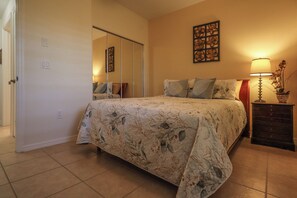 Un dormitorio con cama, mesita de noche, lámpara, espejo y una obra de arte en la pared.