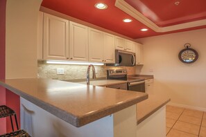 A kitchen with white cabinets, a stainless steel refrigerator, a microwave, and a clock on the wall.