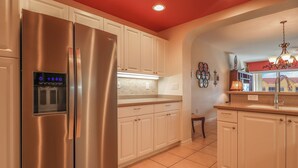 Una cocina con refrigerador de acero inoxidable, armarios blancos, piso de baldosas y techo rojo.