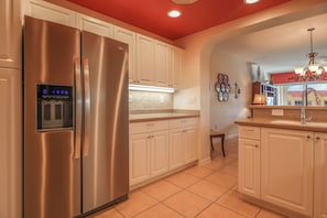 Una cocina con refrigerador de acero inoxidable, armarios blancos, piso de baldosas y techo rojo.
