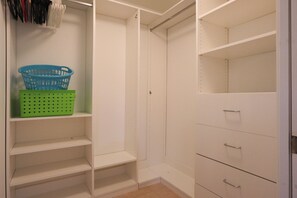 Ein begehbarer Kleiderschrank mit offenen Regalen und Schubladen, ein Korb auf der obersten Ablage und ein Metallgriff an der rechten Schublade.
