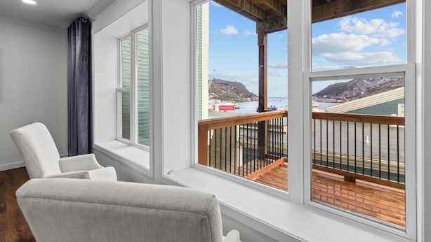 Un balcón con terraza de madera, barandillas blancas y vistas al paisaje costero.