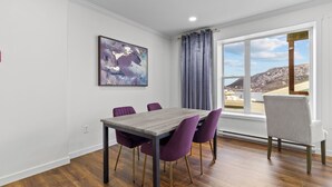 Un comedor con una mesa de madera, sillas moradas, un cuadro en la pared y una ventana con vistas a un paisaje montañoso.