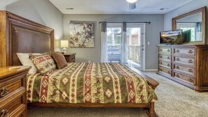 Un dormitorio con una cama grande, un ventilador de techo, un televisor sobre una cómoda y una puerta corrediza de cristal al exterior.