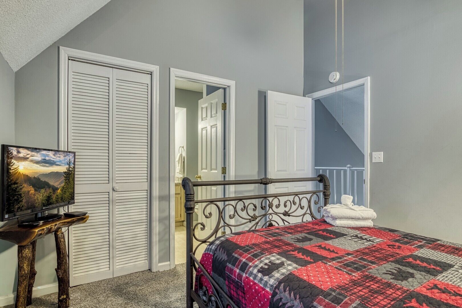 A bedroom with a bed, a TV on a wooden stand, and a wardrobe.