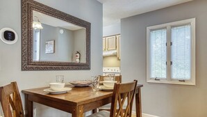 Un comedor con una mesa de madera, cuatro sillas, un espejo grande y decorativo, y una ventana con persianas.