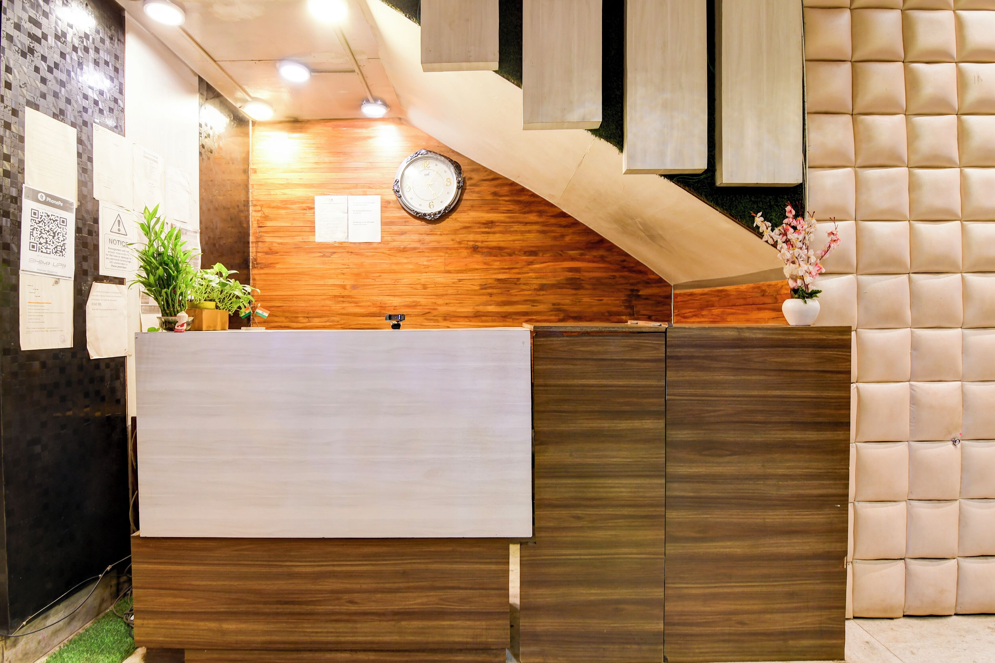 A reception area with a wooden wall, a clock, and a potted plant.