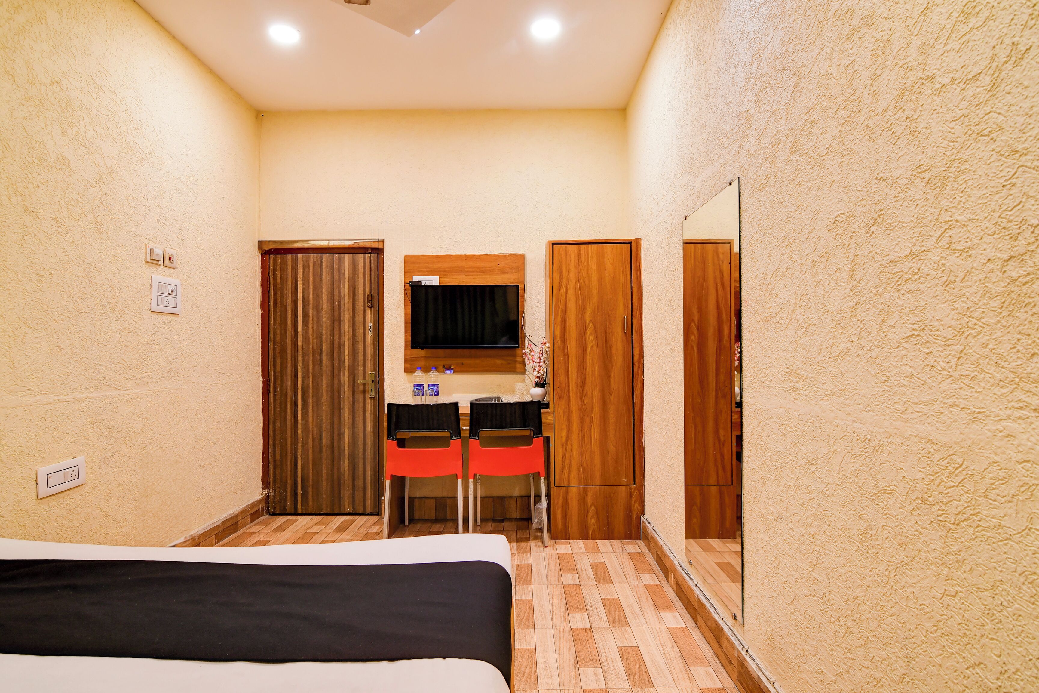 A hotel room with a bed, a small kitchenette, a mirror, and a wooden door.