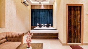 A bedroom with a bed, a wooden headboard, a ceiling fan, a wooden door, and a small table with a vase of flowers. - BRILL MARINA (Kolkata)