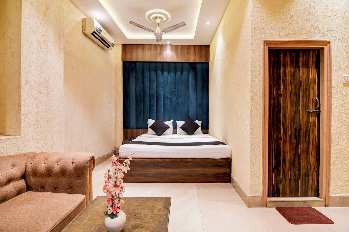 A bedroom with a bed, a wooden headboard, a ceiling fan, a wooden door, and a small table with a vase of flowers.