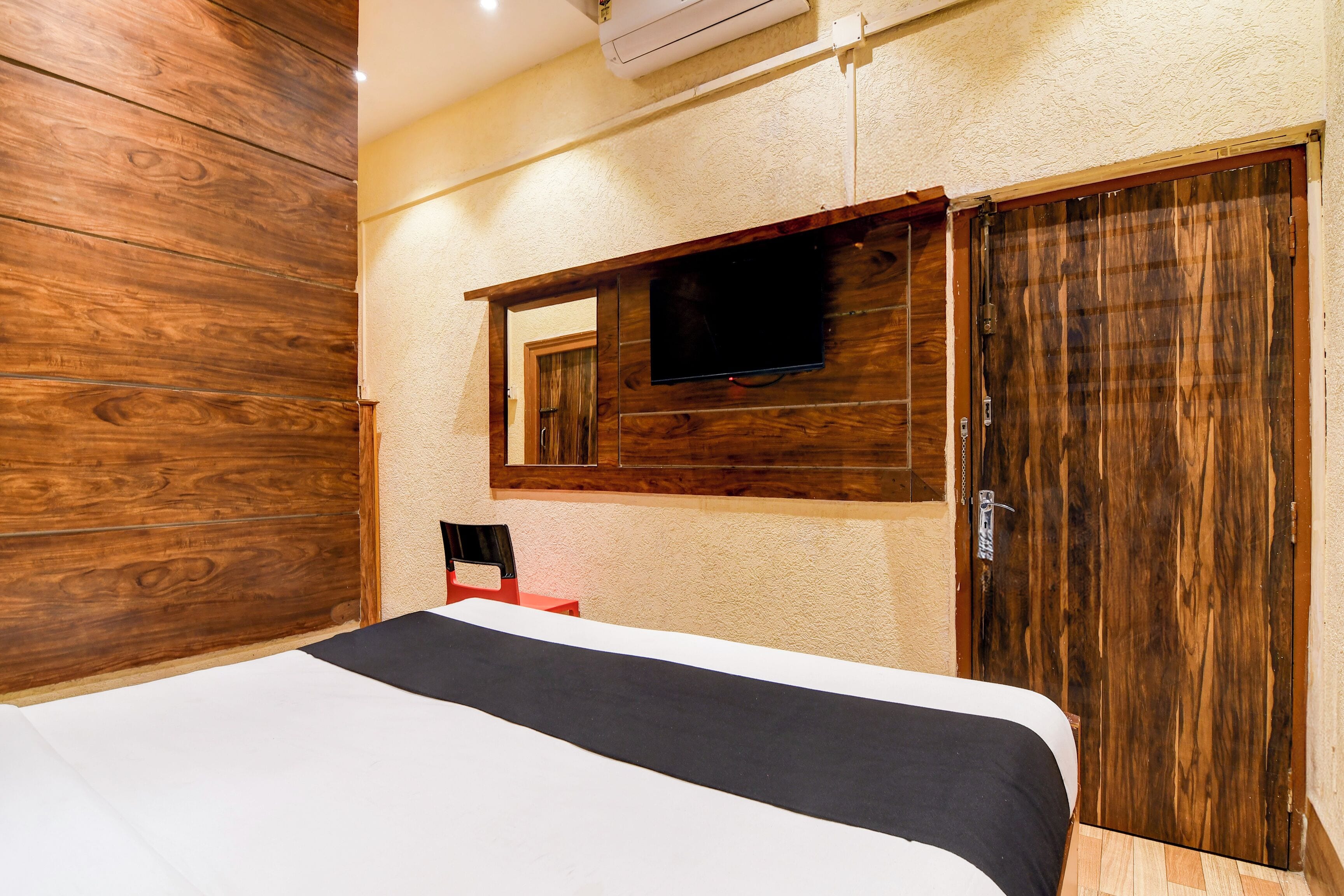 A bedroom with a wooden headboard, a bed with white and black bedding, a television mounted on the wall, and a wooden wardrobe.