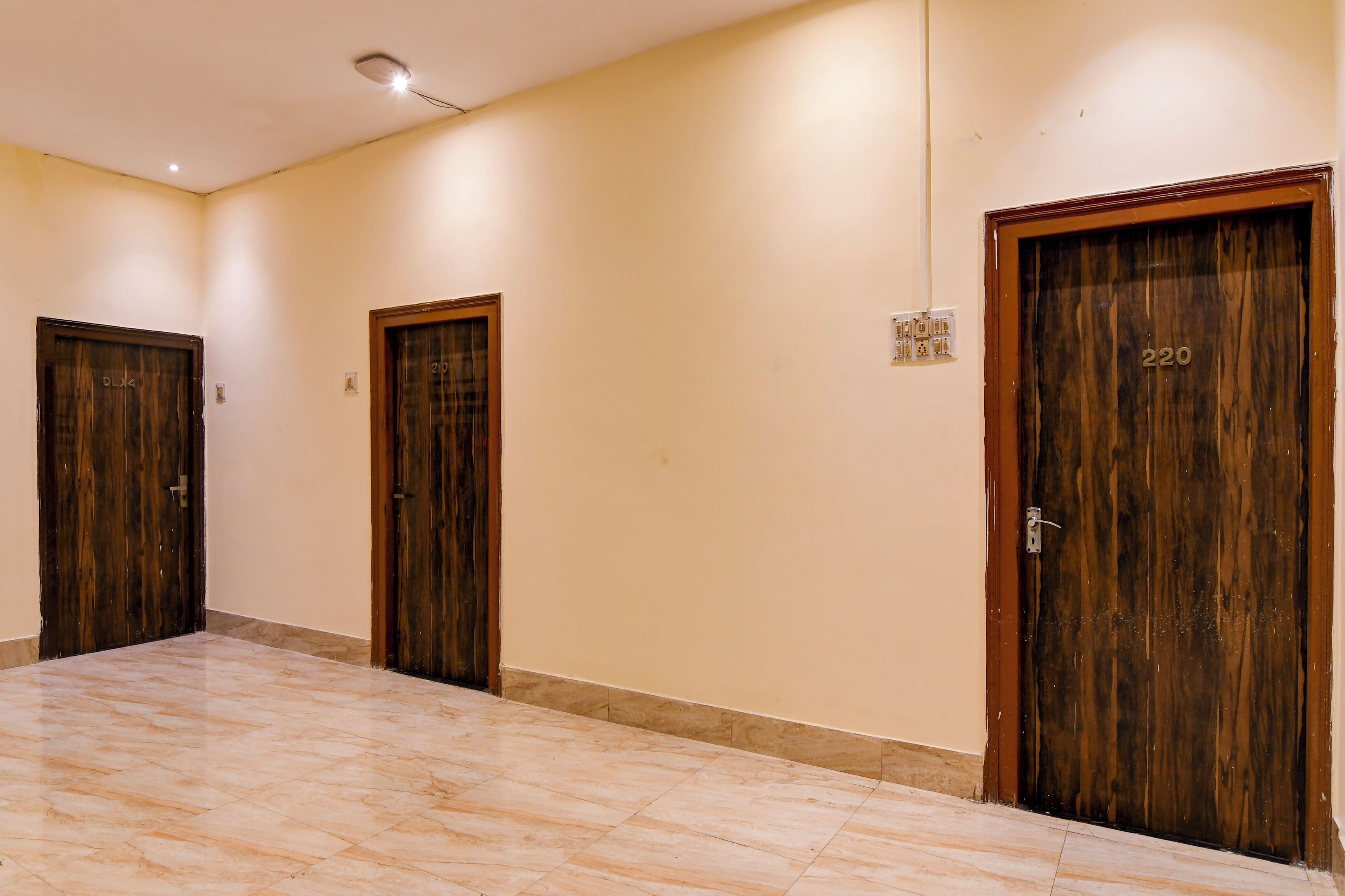 A hallway with three wooden doors, numbered 220, 210, and 211, leading to rooms. The floor is tiled, and the walls are painted a light color.
