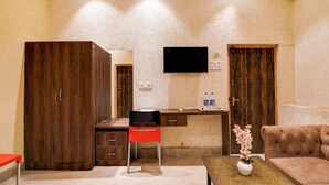 A room with a wooden desk, a red chair, a sofa, and a TV mounted on the wall. - BRILL MARINA (Kolkata)