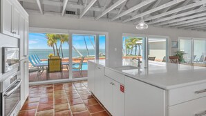 A modern kitchen with large windows, a view of the beach, and a patio area with outdoor seating. - *NEW!*Paradise Point~VIEWS!~Open Water~Dock~Pool! (Marathon)