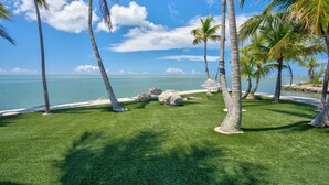 A tropical beach scene with palm trees, a clear blue sky, and a view of the ocean. - *NEW!*Paradise Point~VIEWS!~Open Water~Dock~Pool! (Marathon)