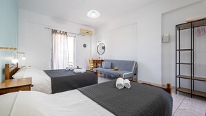 Ein Hotelzimmer mit zwei Betten, einer Schlafcouch, einem Holztischchen, einem Spiegel und einem Kleiderschrank.