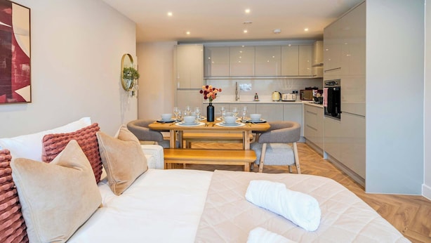 A modern hotel room with a bed, a dining table set for two, and a kitchenette in the background. - FREE Parking, Hi-Speed WiFi,55 Inch 4K TV LongStay (Farnborough)