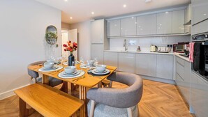 A modern kitchen with grey cabinets, a wooden dining table set for four, and a grey upholstered chair. - FREE Parking, Hi-Speed WiFi,55 Inch 4K TV LongStay (Farnborough)