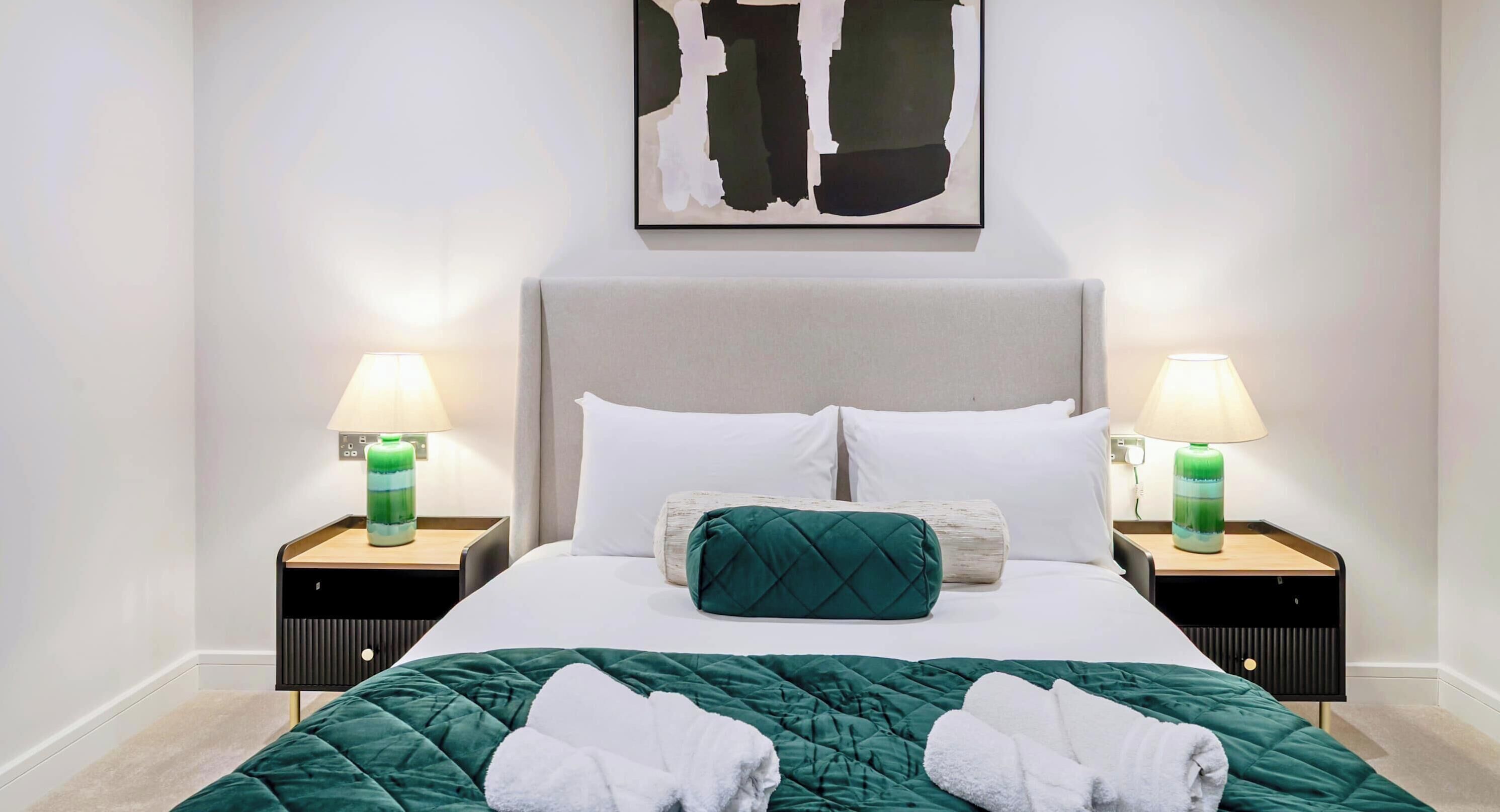 A neatly made bed with a green quilt, white pillows, and two bedside lamps with green bases.