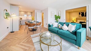 A modern living room with a teal sofa, a glass coffee table, and a dining area with a wooden herringbone floor. - Stunning Flat, Hi-Speed WiFi, 55 Inch 4K TV, Desk (Hampshire)