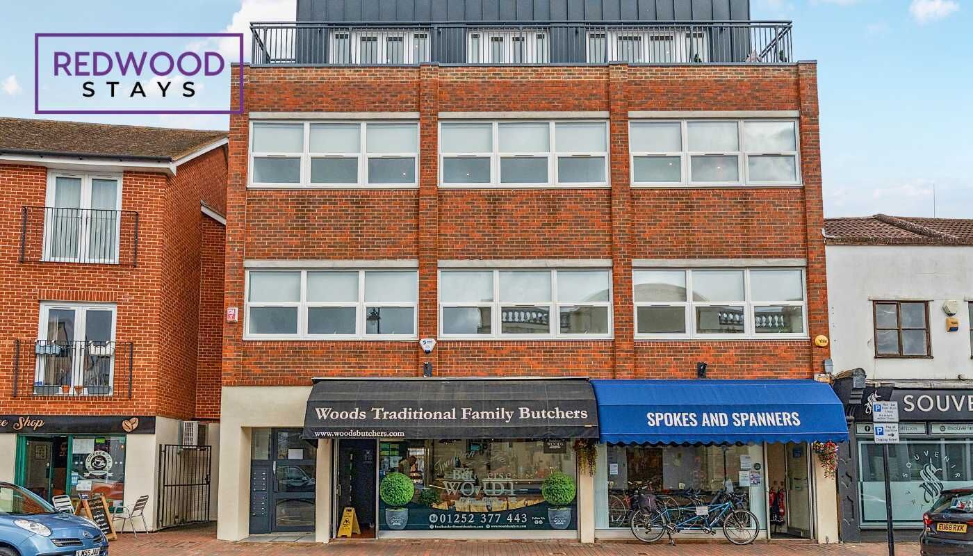 Un edificio de varios pisos con fachada de ladrillo, que alberga comercios como 'Woods Traditional Family Butchers' y 'SPOKES AND SPANNERS'.