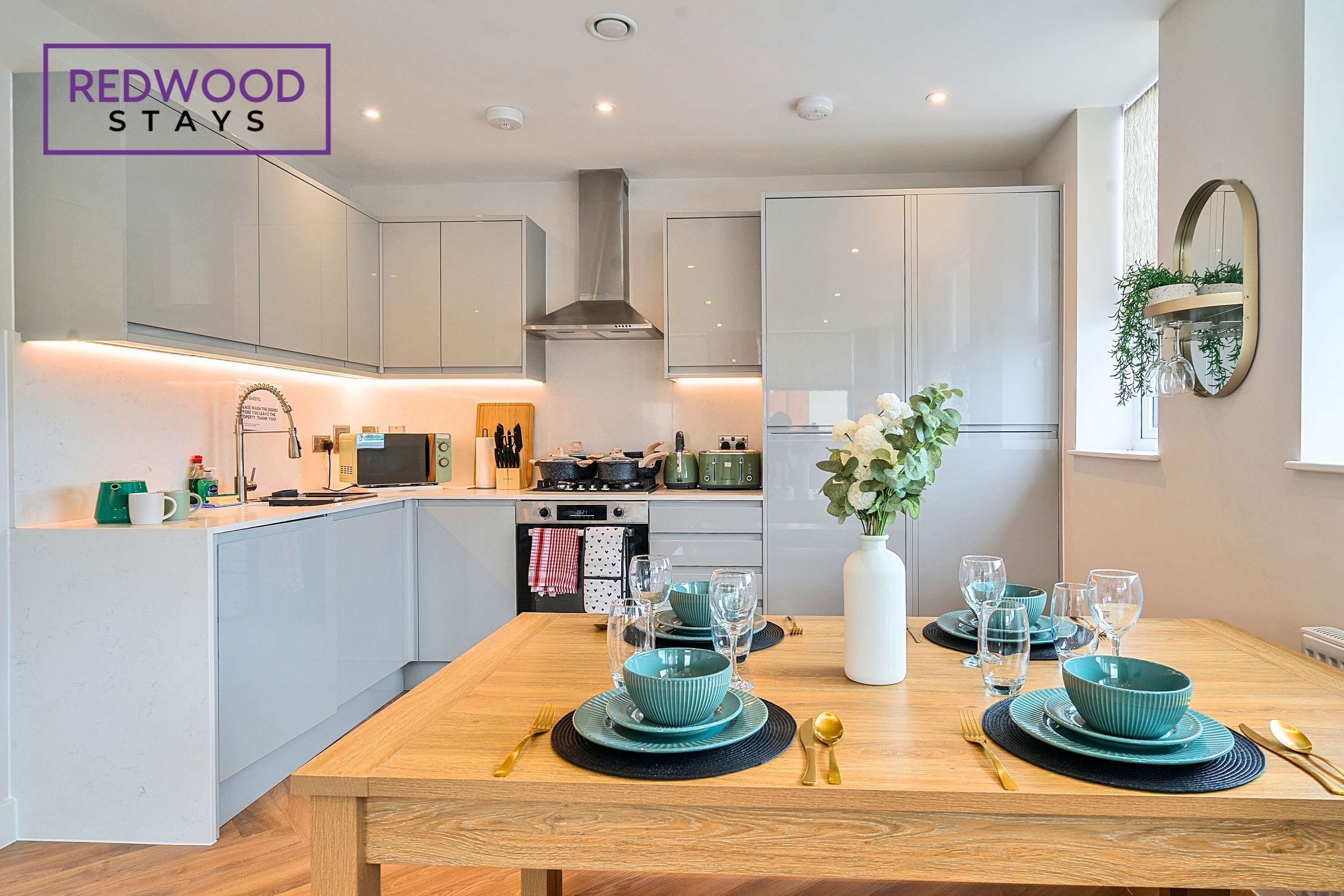 Una cocina moderna con armarios blancos, una isla central y un comedor con vajilla azul turquesa.