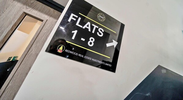 A sign indicating the direction to flats 1-8. - Hi-Speed WiFi, 55 Inch 4K TV, FREE Parking, Desk (Farnborough)