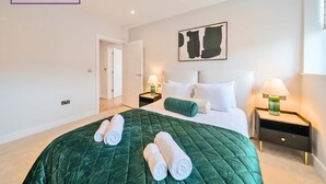 A hotel room with a large bed, green bedding, two bedside tables with lamps, and a painting on the wall.