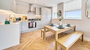 A modern kitchen with white cabinets, a wooden dining table set for four, and a view of the city through the window.