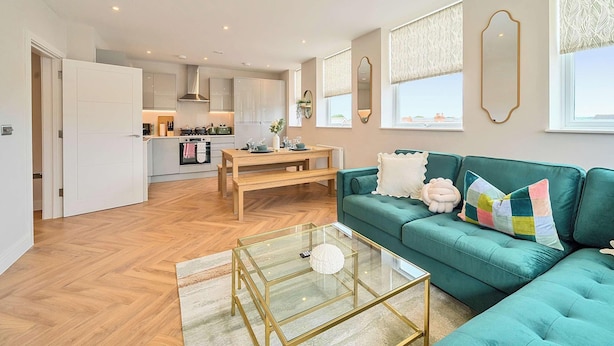 A modern living room with a teal sofa, a glass coffee table, and a wooden dining table.