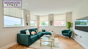 A modern living room with a green sofa, a glass coffee table, and a large window with a view of buildings.