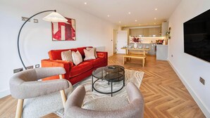 A modern living room with a red sofa, a round coffee table, and a TV mounted on the wall. - Penthouse | FREE Parking | Hi-Speed WiFi | Balcony (Farnborough)