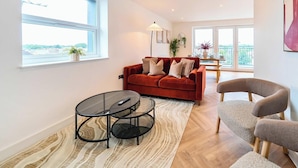 Ein modernes Wohnzimmer mit einem roten Sofa, einem runden Glastisch und einem grauen Sessel.
