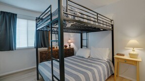 A bunk bed with a wooden frame, a bedside table with a lamp, and a window with curtains.