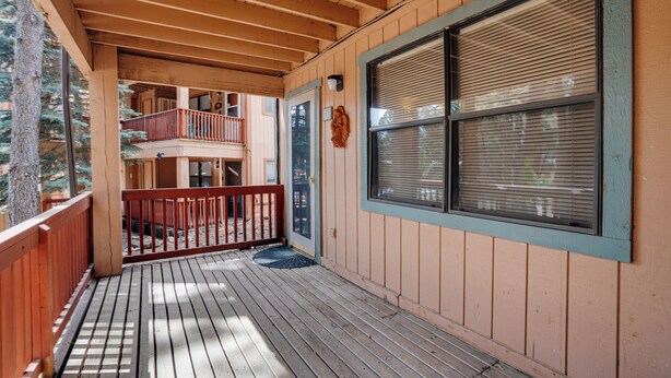 A wooden deck with a red railing, a door with a decorative angel, and a window with blinds.