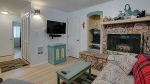 A living room with a television, a stone fireplace, a teal cabinet, and a patterned sofa.