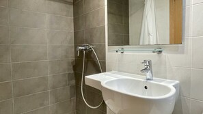 Een badkamer met een wit wastafel, een glazen plank erboven en een douche met een handdouche.