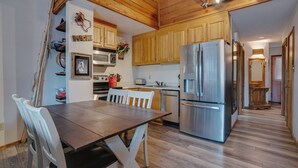 A kitchen with wooden cabinets, a stainless steel refrigerator, a dining table with chairs, and a microwave on the wall. - Condo within walking distance of the Chile Express (Angel Fire)