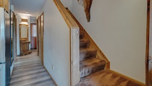 A hallway with a wooden staircase, a mounted animal head, and a refrigerator. - Condo within walking distance of the Chile Express (Angel Fire)