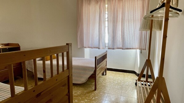 A small, neatly arranged bedroom with a single bed, a wooden crib, and a small table. - APARTAMENTO SAMARIA (Pals)